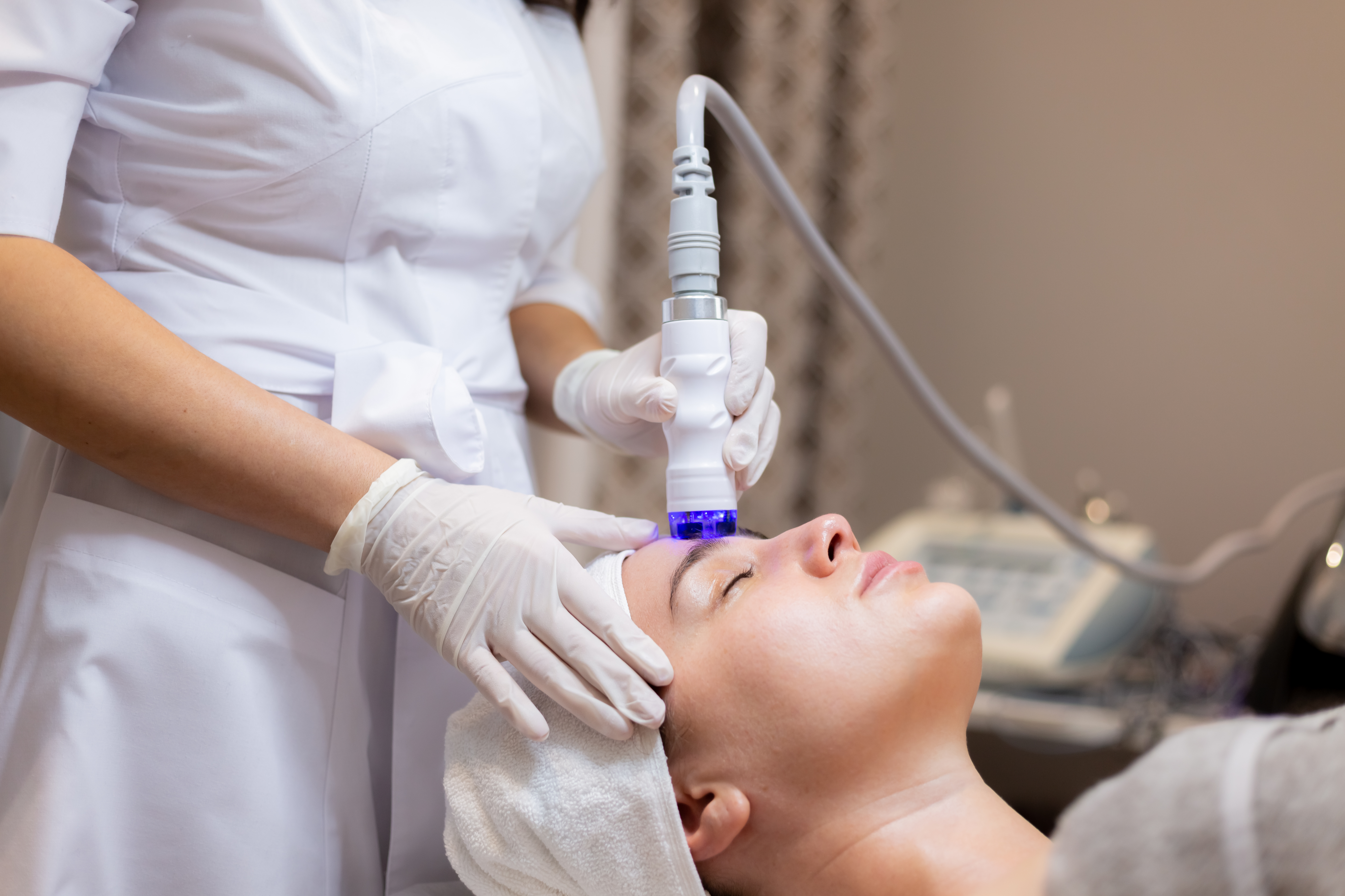 A young beautiful girl lies on the beautician’s table and receives procedures with a professional apparatus for skin rejuvenation and moisturizing